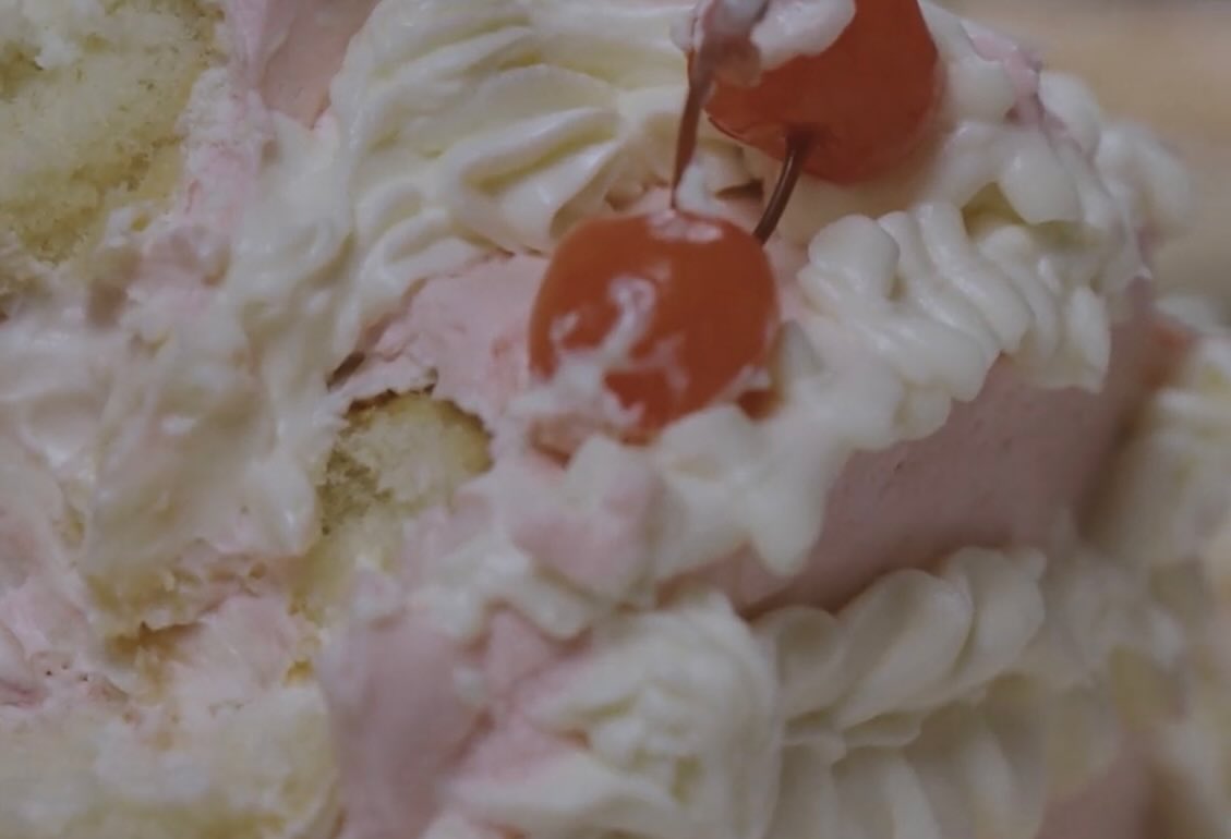 Film still: extreme close-up of a cherry pressed into cake icing
