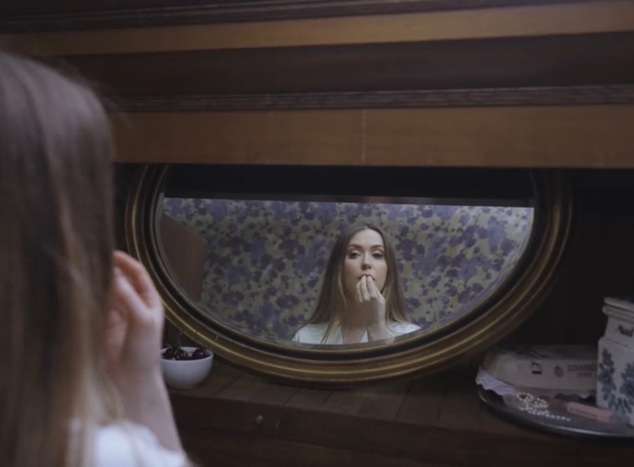 Film still: Dalia reflected in an oval vanity mirror